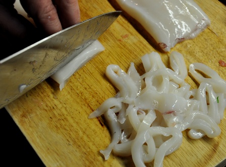 An image of squid being sliced on a chopping baord