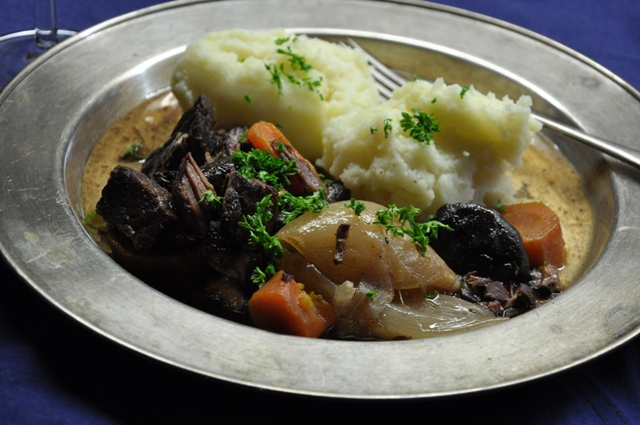 An image of beef bourguignon and vegetables on metal platter