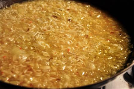 An image of simmering rice, onions and stock in a pan.
