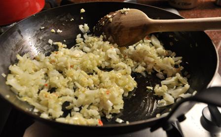 An image of frying onion, garlic and chili in a pan