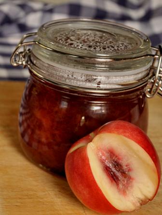 An image of a jar of nectarine jam, with a fresh nectarine on a chopping board