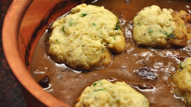 An image of beef stew and dumplings in an earthenware dish