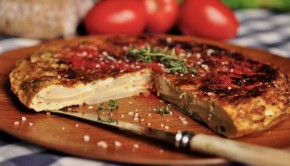 An image of a sliced Spanish tortilla with tomatoes